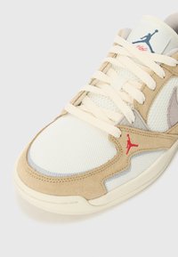 Beige és fehér sneaker, hálós és velúrból készült anyaggal, krémszínű fűzőkkel és piros logó részletekkel. Alacsony profilú kialakítással és kerek orral rendelkezik.