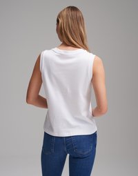 White sleeveless top with a round neckline, soft cotton material, and a relaxed fit. Paired with blue denim jeans featuring back pockets.