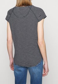 Kortärmad topp i svart och vitt randig design med rundad nederkant och raglanärmar, tillverkad av mjukt tyg. Bakifrån syns subtila sömnadsdetaljer.