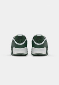 Zaļi un balti Nike Air sporta apavi ar teksturētu virsu, redzamu logo un izturīgu zoli. Aizmugures skats izceļ unikālu papēža dizainu.