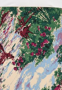 Un tessuto multicolore presenta un design floreale con foglie verdi e fiori rosa su uno sfondo azzurro, evidenziando un motivo testurizzato.