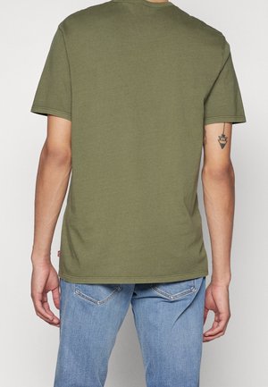T-shirt in cotone verde oliva con maniche corte, scollatura rotonda e taglio dritto. Presenta un piccolo etichetta rossa sul bordo.