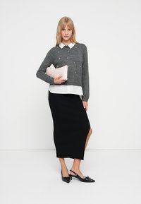 Grå genser med perleaccenter over en hvit skjorte med krage, kombinert med et svart ribbestrikket midiskjørt og en rosa clutch. Sorte spisse sko.