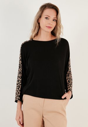 Black long-sleeve top with leopard print accents on sleeves. Soft, smooth fabric; relaxed fit; round neckline; paired with beige trousers.