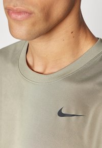 Oliwkowa koszulka z okrągłym dekoltem wykonana z mieszanki bawełny, z czarnym logo Nike na lewej piersi. Widoczny prążkowany dekolt i gładka tekstura.