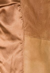 Brunt læder og satin stof i et patchworkdesign, der viser forskellige teksturer og overflader, med synlige syninger langs sømmene.