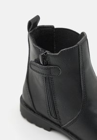 Bottine en cuir noir avec fermeture éclair et détails cousus, dotée d'une languette et d'une surface texturée.