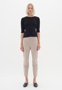 Černý žebrovaný pletený top s krátkým rukávem, kombinovaný s béžovými tailored kalhotami a černými plochými botami. Jednoduchá, přiléhavá silueta.