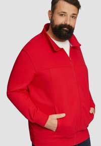Rode zip-up sweatshirt van een zachte stof met een hoge kraag. Beschikt over lange mouwen, zijzakken en een rits aan de voorkant.