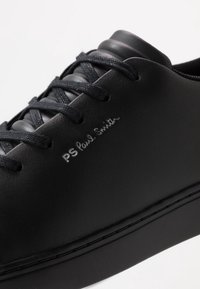 Baskets en cuir noir avec lacets noirs et languette rembourrée, avec le texte "PS Paul Smith" sur le côté près des lacets.