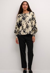 Blus med abstrakt mönster i svart och kräm, rund halsringning och voluminösa ärmar, matchad med svarta skräddarsydda byxor och loafers.