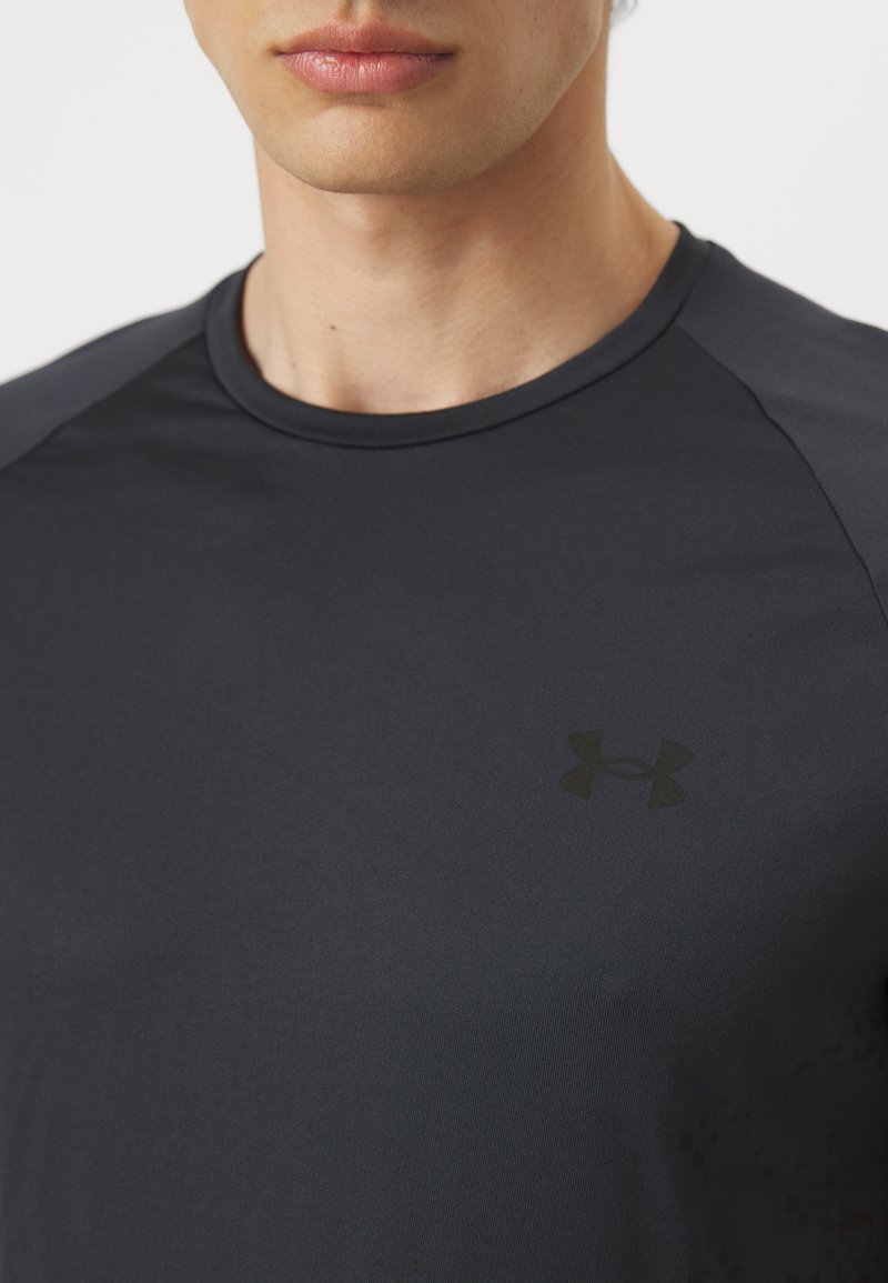 Camiseta deportiva de color gris oscuro, hecha de una tela suave y ligera. Presenta un cuello redondo y un sutil logo negro en el pecho.