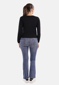 Maglione nero a maniche lunghe in maglia con scollatura tonda, abbinato a jeans a zampa d'elefante blu e sneakers bianche, visto da dietro.