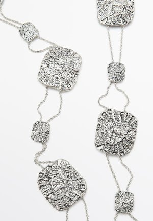 Metalowa naszyjnik z teksturowanymi srebrnymi ogniwami oraz różnokształtnymi, wzorzystymi zawieszkami. Gładka powierzchnia o lustrzanym wykończeniu.