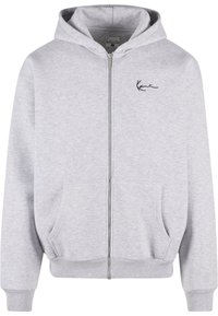 Grå hettegenser med glidelås laget av mykt stoff, med en frontglidelås, to sidelommer og en svart brodert logo på brystet.