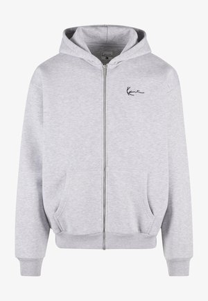Sudadera gris con cremallera fabricada en un tejido suave, que cuenta con una cremallera frontal, dos bolsillos laterales y un logotipo bordado en negro en el pecho.
