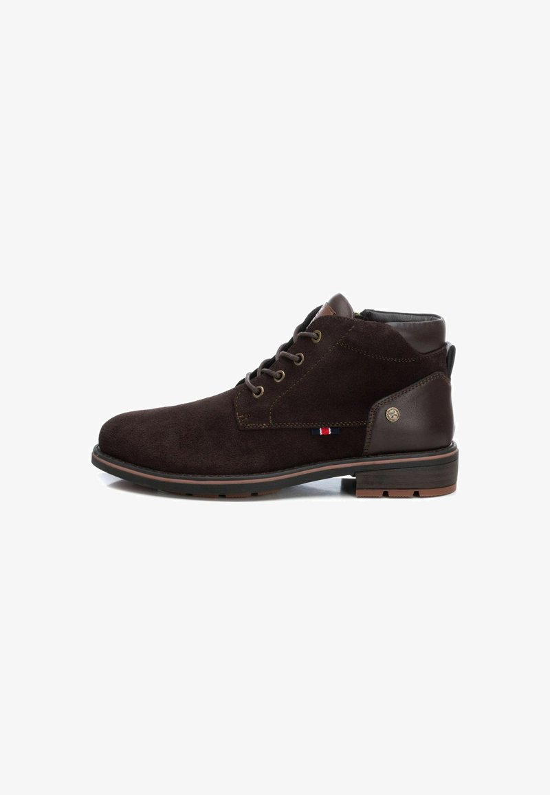 Botas de tobillo de ante marrón con un acento de cuero marrón liso, punta redonda y cinco ojetes para los cordones. Presenta un pequeño logo y una suela en contraste.