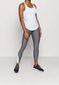 Top sportivo azzurro chiaro con scollatura rotonda e spalline sottili abbinato a leggings grigi scuri con pannello laterale azzurro chiaro. Scarpe da corsa nere.