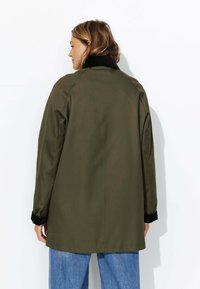 Manteau vert olive avec un col noir, à la coupe décontractée, manches longues et design mi-long, fabriqué en tissu doux.