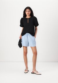 Black textured top with short puff sleeves and keyhole detail, paired with light blue striped shorts. Beige flat shoes and a black bag.