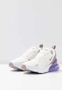 Zapatillas Nike Air Max con parte superior de malla blanca, acentos en púrpura claro y una unidad de aire visible en el talón, con suela de goma texturizada.