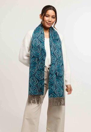 Teal scarf with a swirl pattern, made from soft fabric, featuring fringe detailing at the ends and a small logo tag.