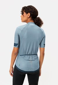 Le maillot de cyclisme bleu clair présente des manches courtes, un design texturé et une poche arrière avec un élastique à l'ourlet. Le logo de la marque est visible.