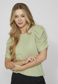 Lichtgroene, textuurgegeven top met korte puff sleeves en een ronde halslijn, voorzien van een subtiel patroon en een ontspannen pasvorm, gecombineerd met zwarte onderkleding.