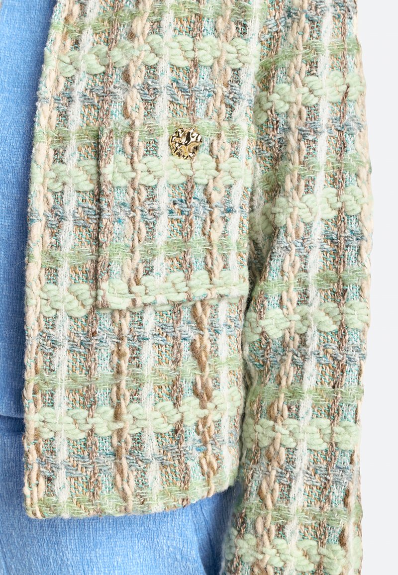Strickjacke in grünen, blauen und beigen Farbtönen mit einem strukturierten Gewebemuster; verfügt über einen dekorativen goldfarbenen Knopf auf der Vorderseite.