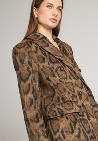 Dubbelknoop blazer in bruin en zwart luipaardprint. Gemaakt van gestructureerde stof met geschulpte revers en voorkeurszakken. Voorzien van donkere knopen.