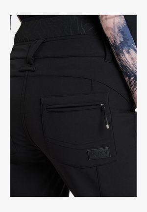 Schwarze Sporthosen mit einer Reißverschlusstasche, strukturiertem Stoff und einem Logopatch. Das Design umfasst gestochene Details und eine figurbetonte Silhouette.