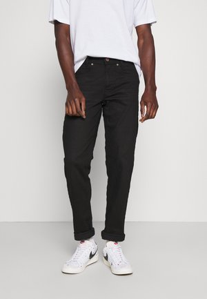 Jeans de mezclilla negra con corte recto, cinco bolsillos y sutiles detalles de costura, combinados con zapatillas blancas y una camiseta holgada.