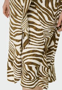 Handen die de zoom vasthouden van een bruin en witte rok met zebra-patroon, gemaakt van zachte, vloeiende stof en met een gelaagd ontwerp.