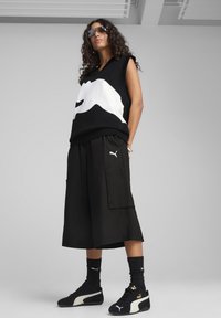 Gilet senza maniche a maglia bianco e nero con grafica di montagna, abbinato a pantaloni cargo neri. Presenti sneakers e calze nere.