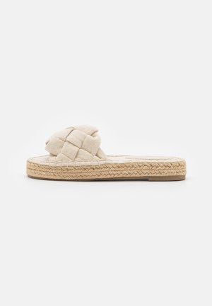 Sandale slip-on tissée beige avec une partie supérieure en textile tressé et une semelle en jute. Design plat avec des détails texturés et une apparence minimaliste.