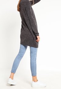 Grå stickad lång tröja med en lös passform, kombinerad med ljusblå smala jeans och vita sneakers. Slät textur och avslappnad design.