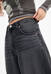 Black denim jeans with a fitted waist, silver button closure, and copper rivets. Features classic 5-pocket style and subtle texture.