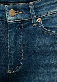 Ciemnoniebieskie dżinsy z denimu z pomarańczowym przeszyciem, metalowym guzikiem do zapięcia oraz przednią kieszenią. Gładka tekstura i klasyczny design z pięcioma kieszeniami.