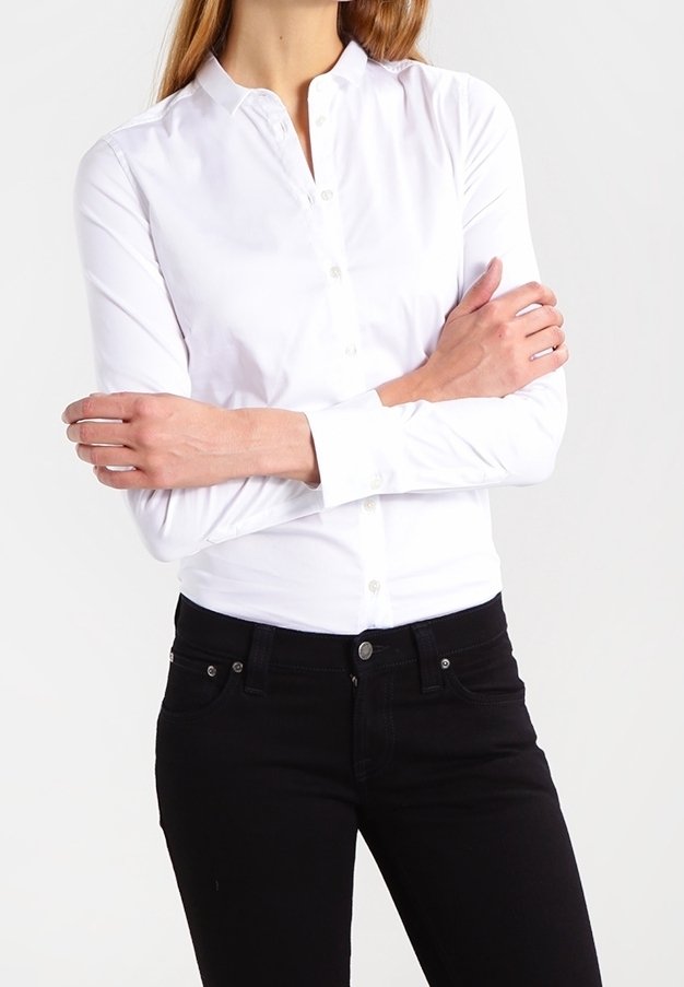 Camisa blanca de botón con cuello, de mangas largas y fabricada en un tejido suave y ligero; combinada con unos jeans ajustados negros.