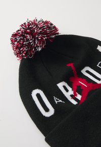 Black knit beanie featuring a multicolored pom-pom on top, with white lettering and a red silhouette design on the front.