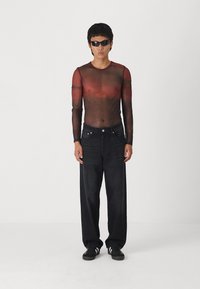 Sheer long-sleeve top in gradient red to black, paired with loose black denim pants and black sneakers. Sunglasses complete the look.
