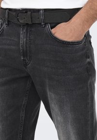 Zwarte denim jeans met een lichte vervaging en een vijf-pocket ontwerp, aangevuld met een zwarte riem met een rechthoekige gesp.