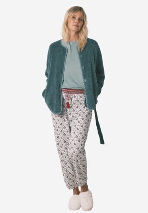 Teal fuzzy cardigan with round buttons, paired with patterned white pants featuring floral designs and a red tie waist. White slippers complete the look.