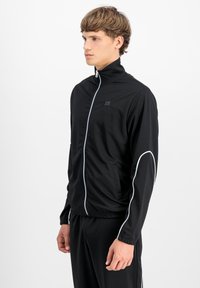 Juodas užtrauktukas džemperis, pagamintas iš lygaus audinio, turi baltas detales ant rankovių ir aukštą apykaklę, su šoniniais kišenėmis patogumui.