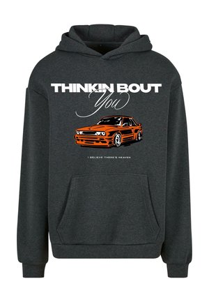 Sudadera gris con un bolsillo frontal. Presenta un gráfico de un coche naranja y un texto blanco que dice "PENSANDO EN TI" y "CREO QUE HAY CIELO."
