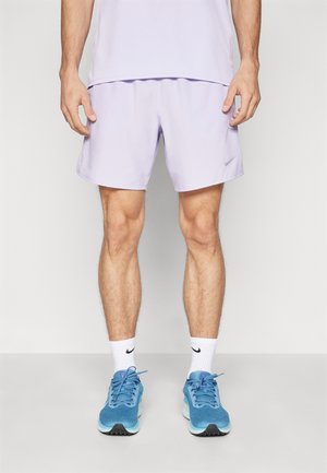 Pantalones cortos deportivos de lavanda claro con cintura elástica y un sutil logo de Nike. Combinados con zapatillas azules y calcetines blancos.