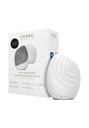 Elegant hvid 5-i-1 sonisk ansigtsbørste med struktureret silikoneoverflade, stående ved siden af sin hvide emballageæske med produktdetaljer.