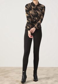 Langsleeve top met een gedraaide halslijn in een bruin en zwart abstract patroon; gecombineerd met zwarte aansluitende leggings en enkellaarsjes.
