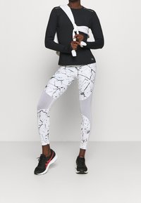 Svart långärmad topp med vit rund hals och bakakcenter; vita tights med ett svart abstrakt mönster; svarta sneakers med röda detaljer.