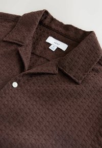 Brown textured shirt with a collar, featuring a subtle woven pattern, a white button, and a tag labeled "NEXT" in size M.